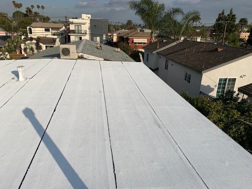 White flat roof with long seams and neighboring homes in the background