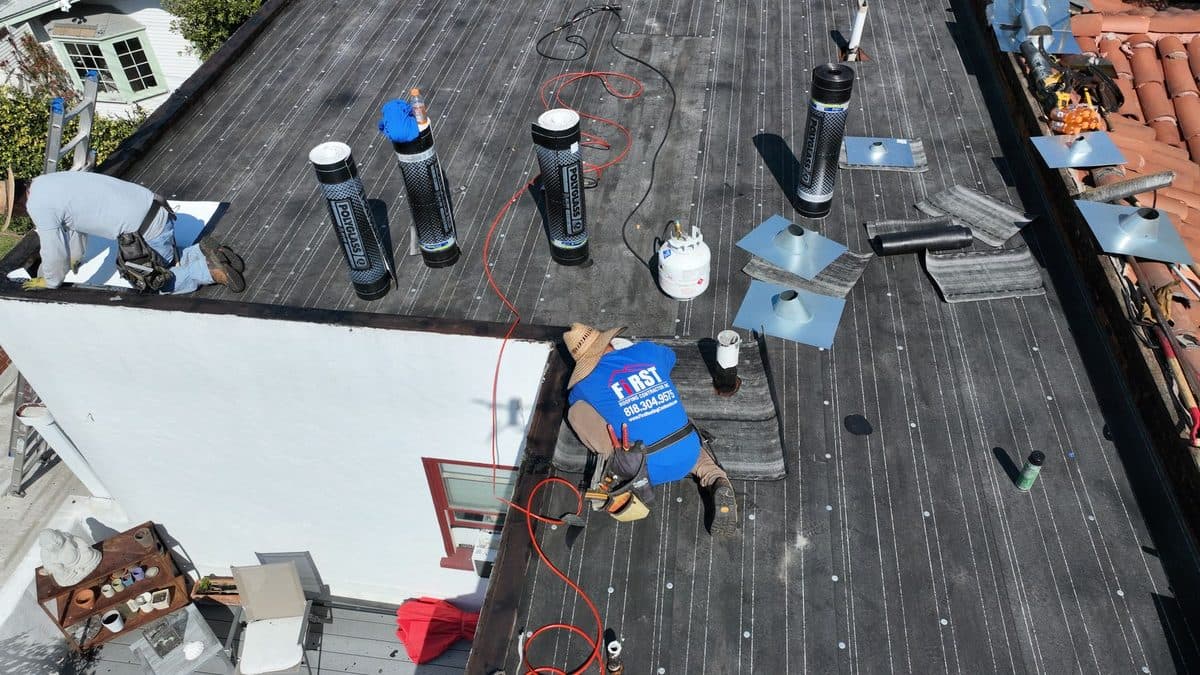 Aerial view of crew members working on a dark flat roof beside a white wall