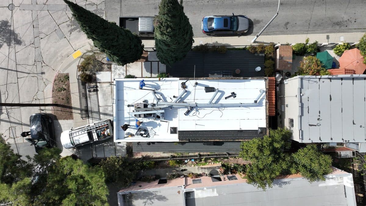 Top-down aerial view of a narrow white flat roof with rooftop piping and equipment