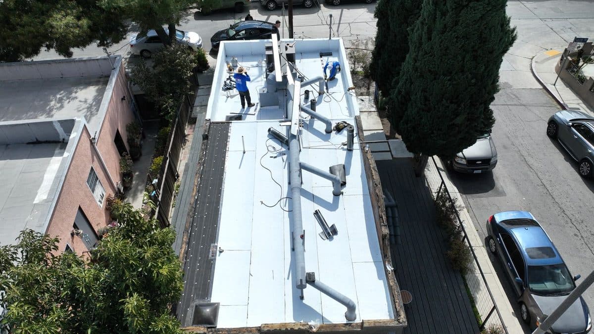 Aerial view of a long narrow flat roof with crew members and rooftop piping