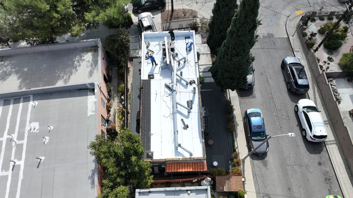 Aerial view of a long narrow white flat roof beside a street and a neighboring gray roof