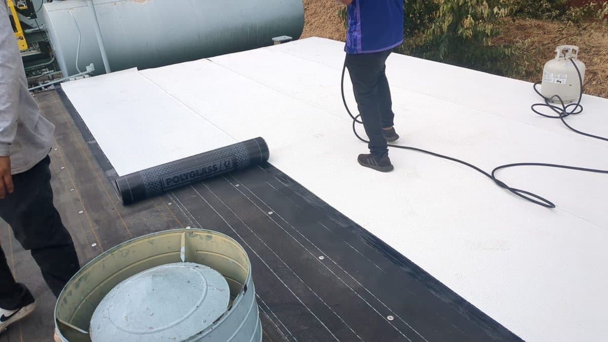 Roll of roofing material on a flat roof beside a rooftop vent