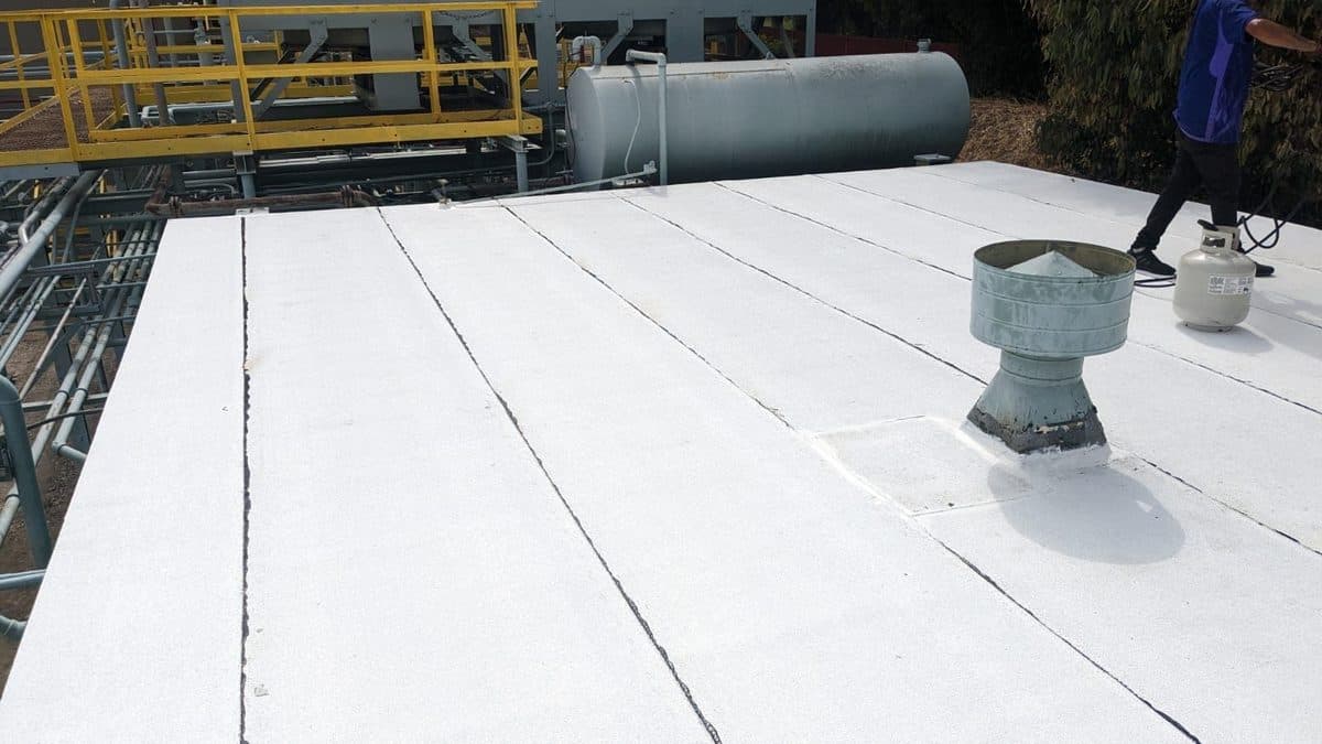 White flat roof with a vent and a propane tank beside industrial equipment
