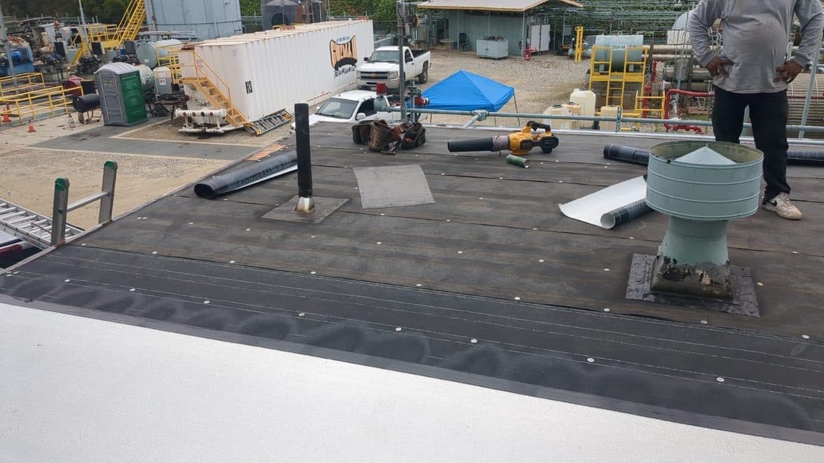 Dark roof deck with a vent, roofing rolls and tools before the white surface is installed