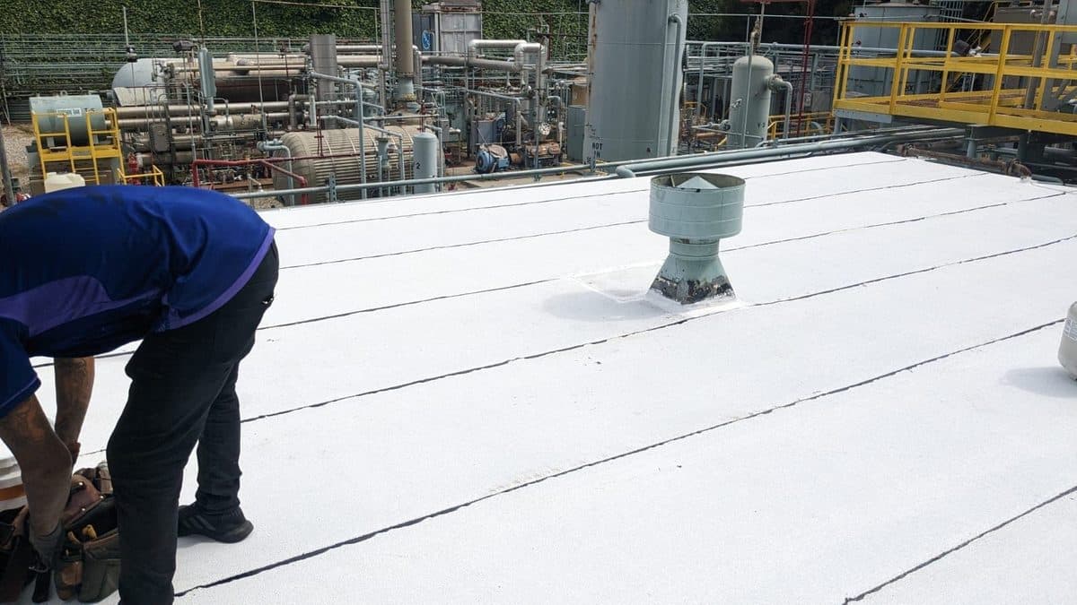 Crew member bending over a white flat roof next to a vent in an industrial area