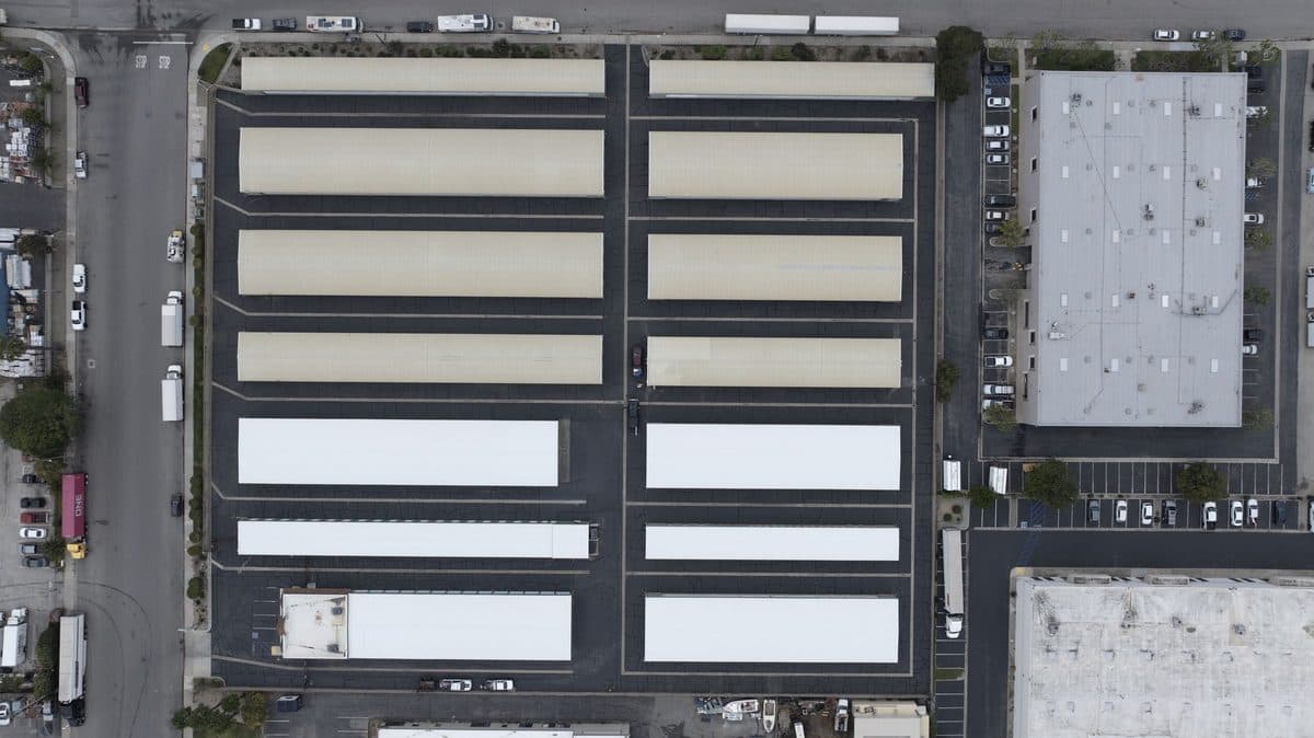 Top-down aerial view of an industrial site with rows of long building roofs, several with white surfaces