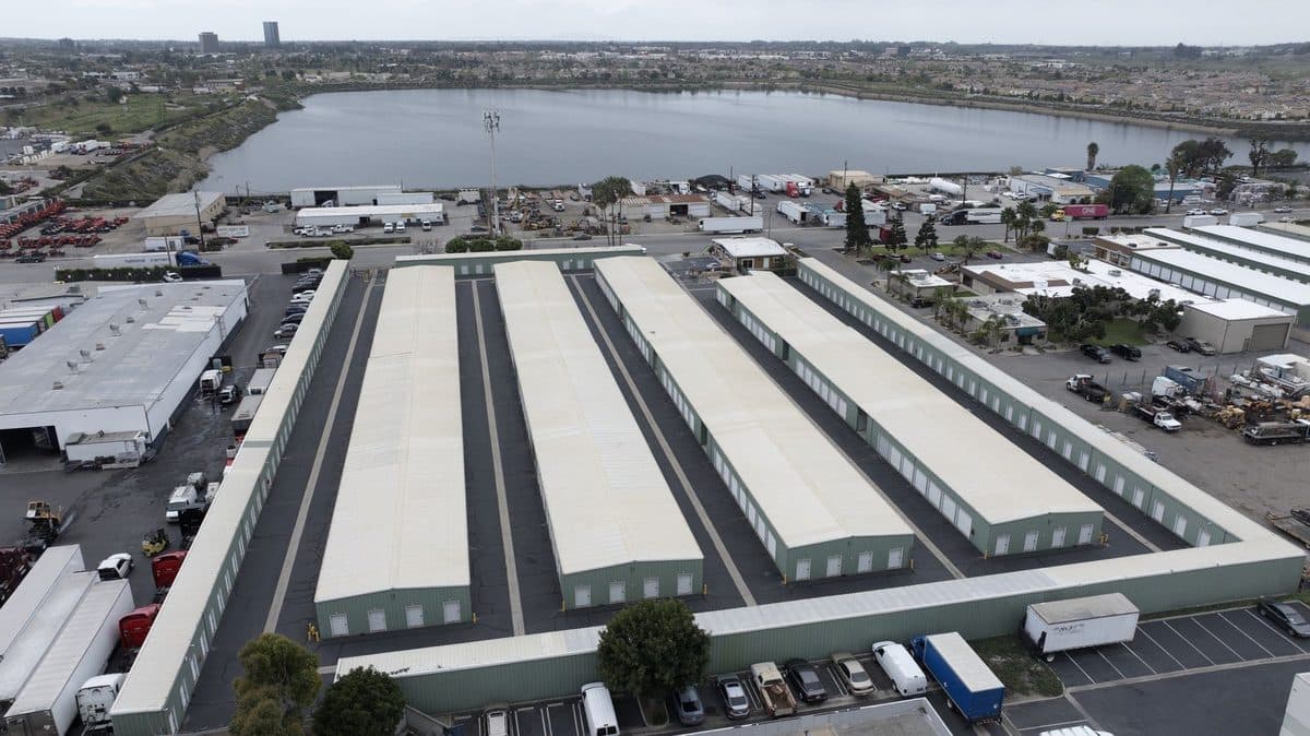 Aerial view of four long storage building roofs with a lake in the background