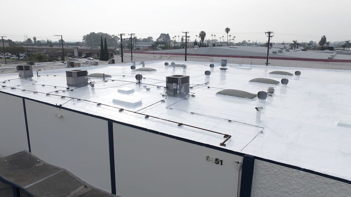 Close view of a white flat roof with rooftop units, skylights and turbine vents