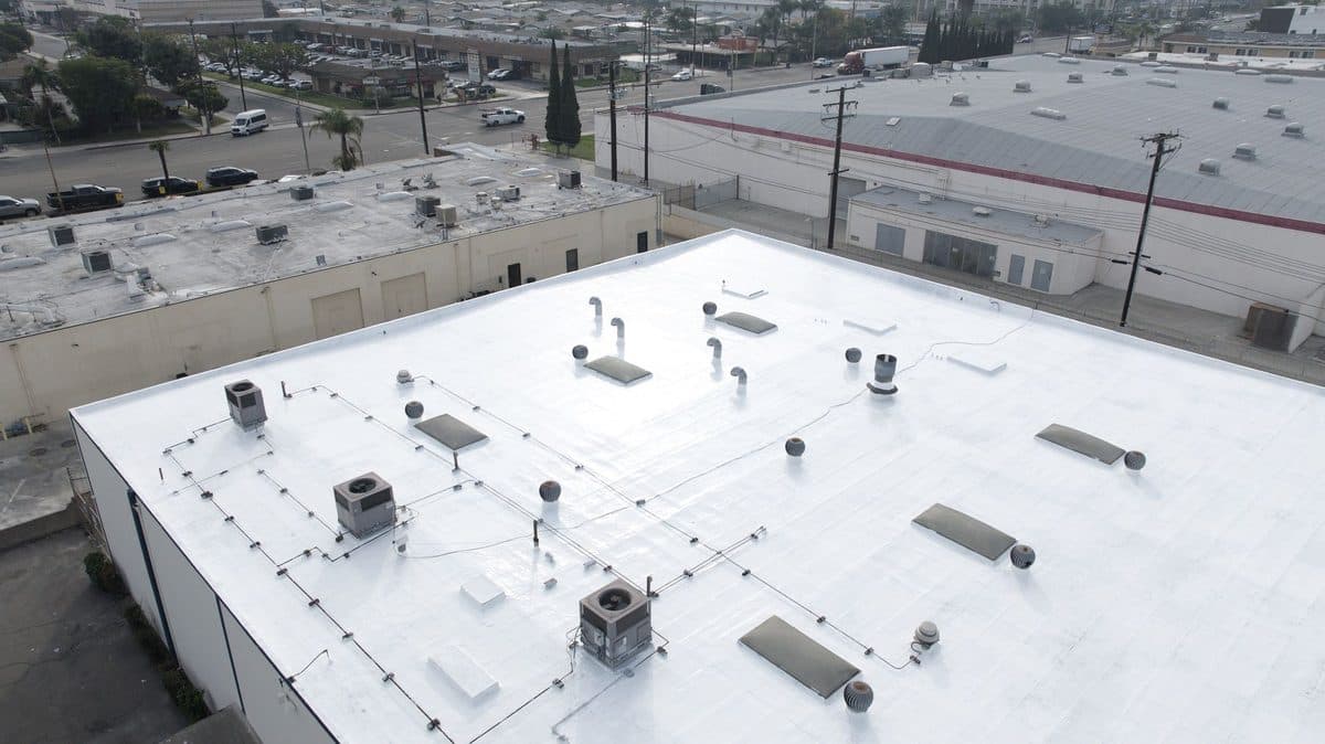 Aerial view of a white commercial flat roof with rooftop units and skylights
