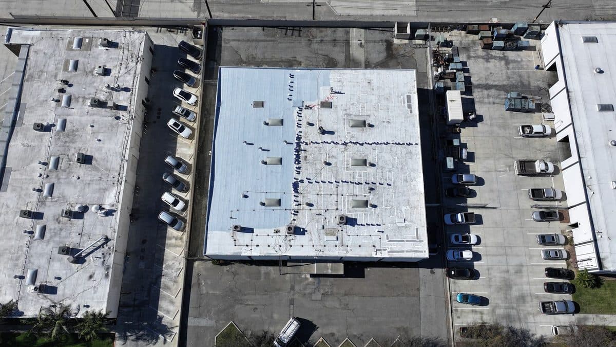 Angled aerial view of a commercial flat roof that is partly white, beside a parking lot