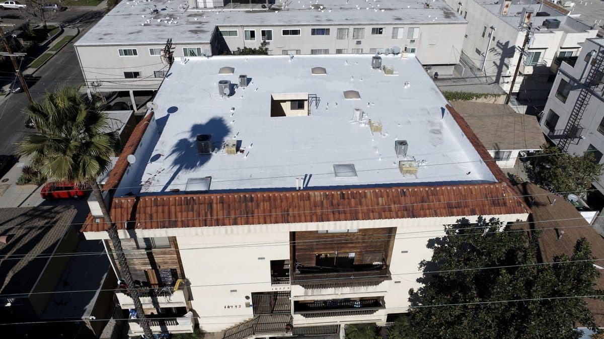 Aerial view of an apartment building with a white flat roof and a clay tile edge