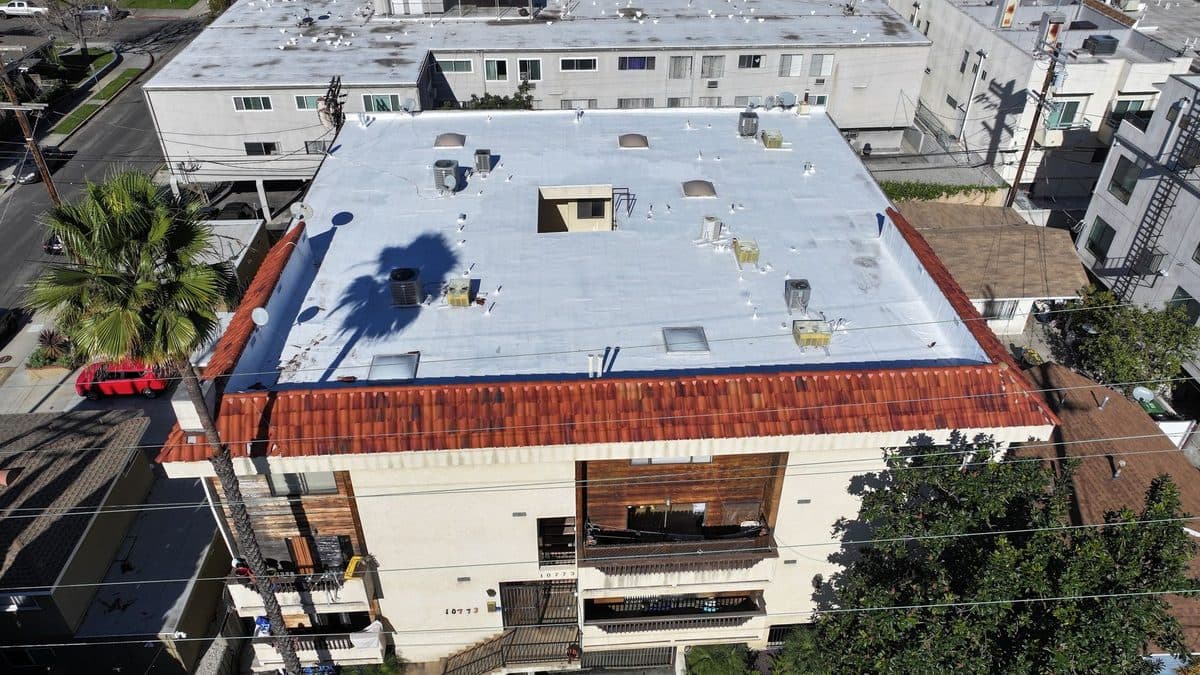 Aerial view of an apartment building with a white flat roof and a clay tile edge, with a palm tree
