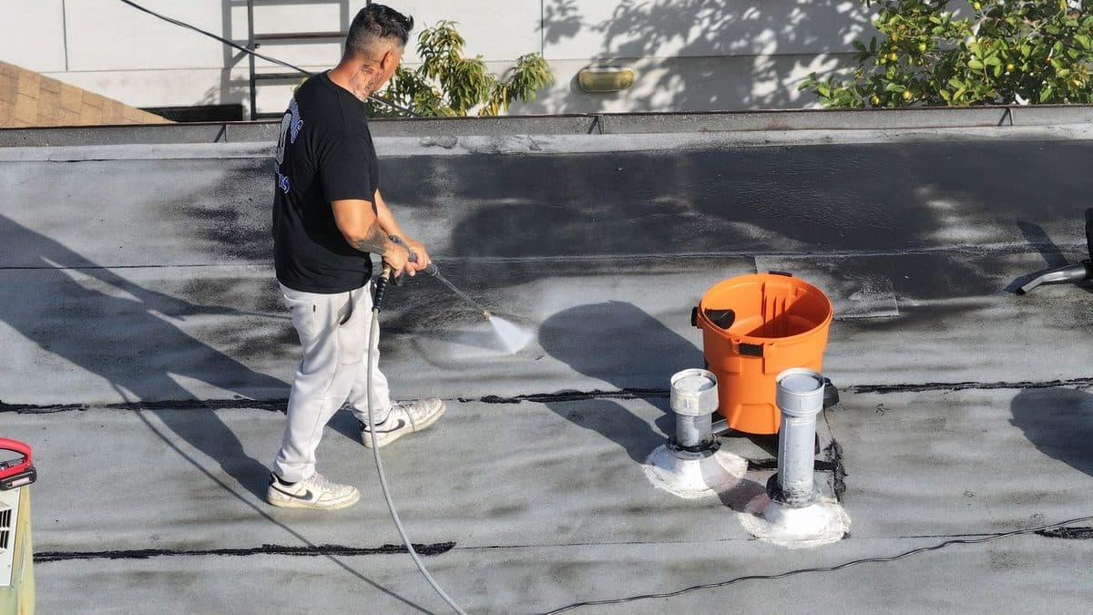 Crew member pressure washing a flat roof around two pipe vents
