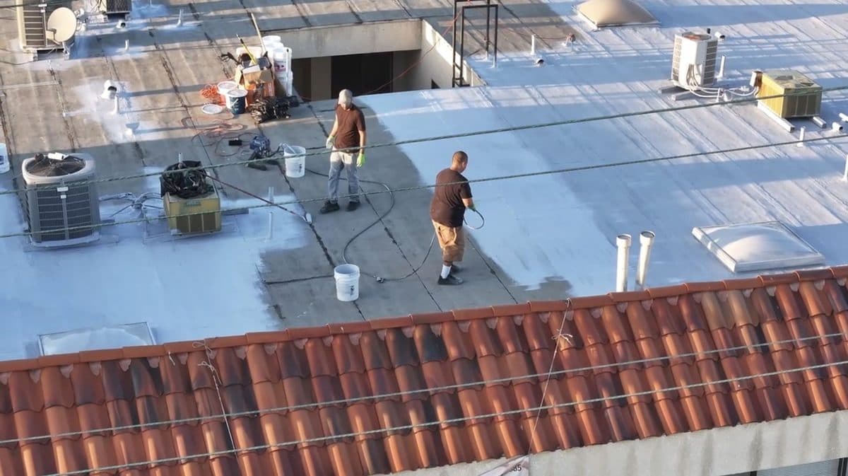Crew members working on an apartment building flat roof beside a clay tile edge
