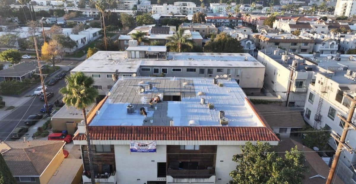 Aerial view of an apartment building with a partly white flat roof and a clay tile edge
