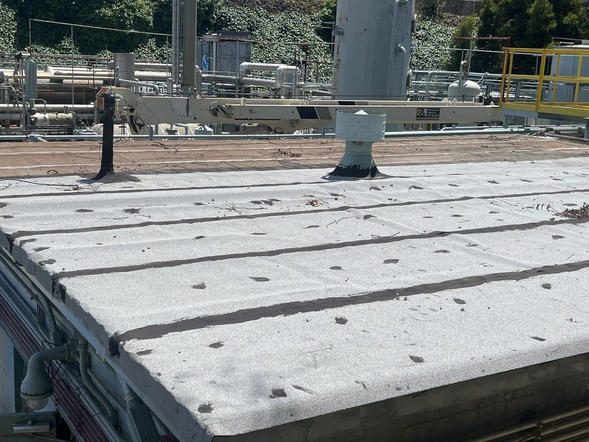 Close view of a flat roof surface with seams and a vent at an industrial site