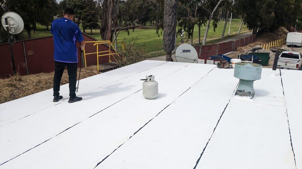 Crew member on a white flat roof beside a propane tank and a vent
