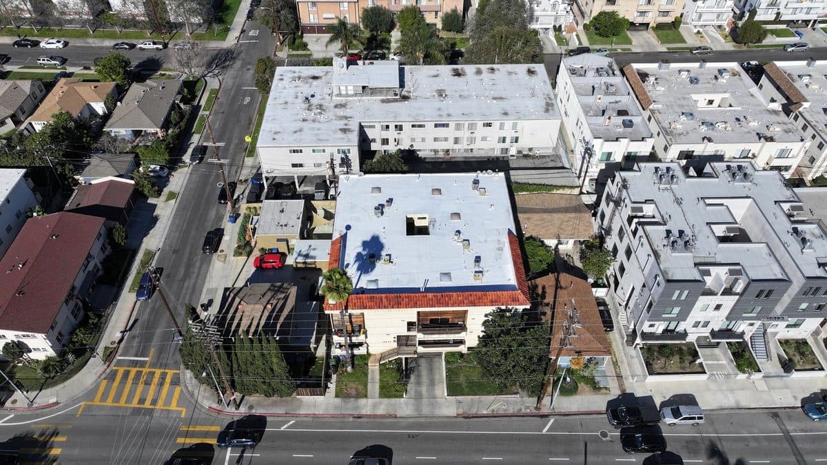 Aerial view of an apartment building with a partly white flat roof and a clay tile edge