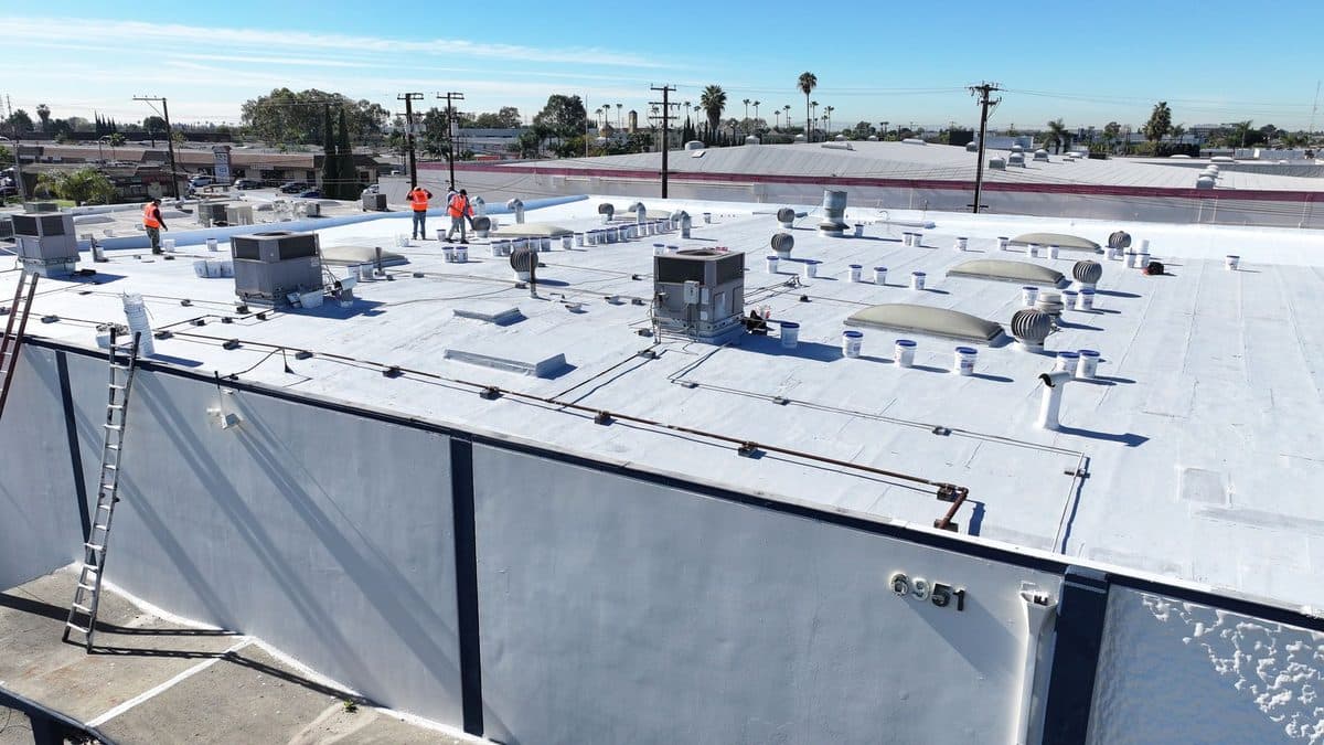 Crew members on a commercial flat roof with rooftop units and a ladder