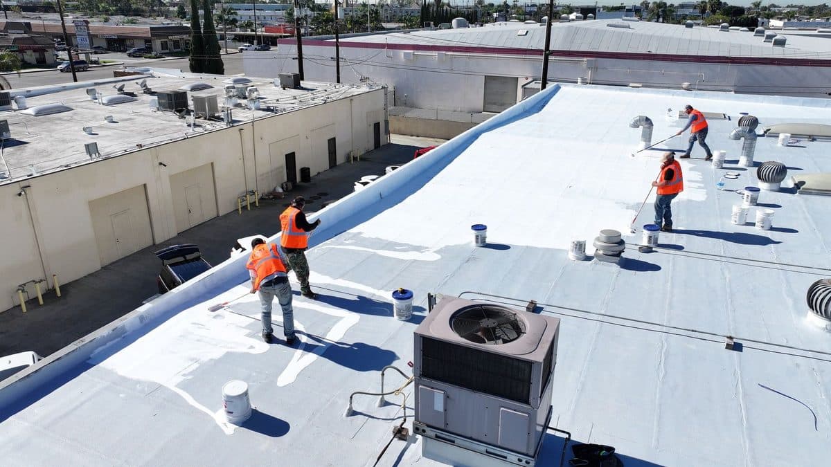 Crew members working on a white flat roof beside a rooftop unit