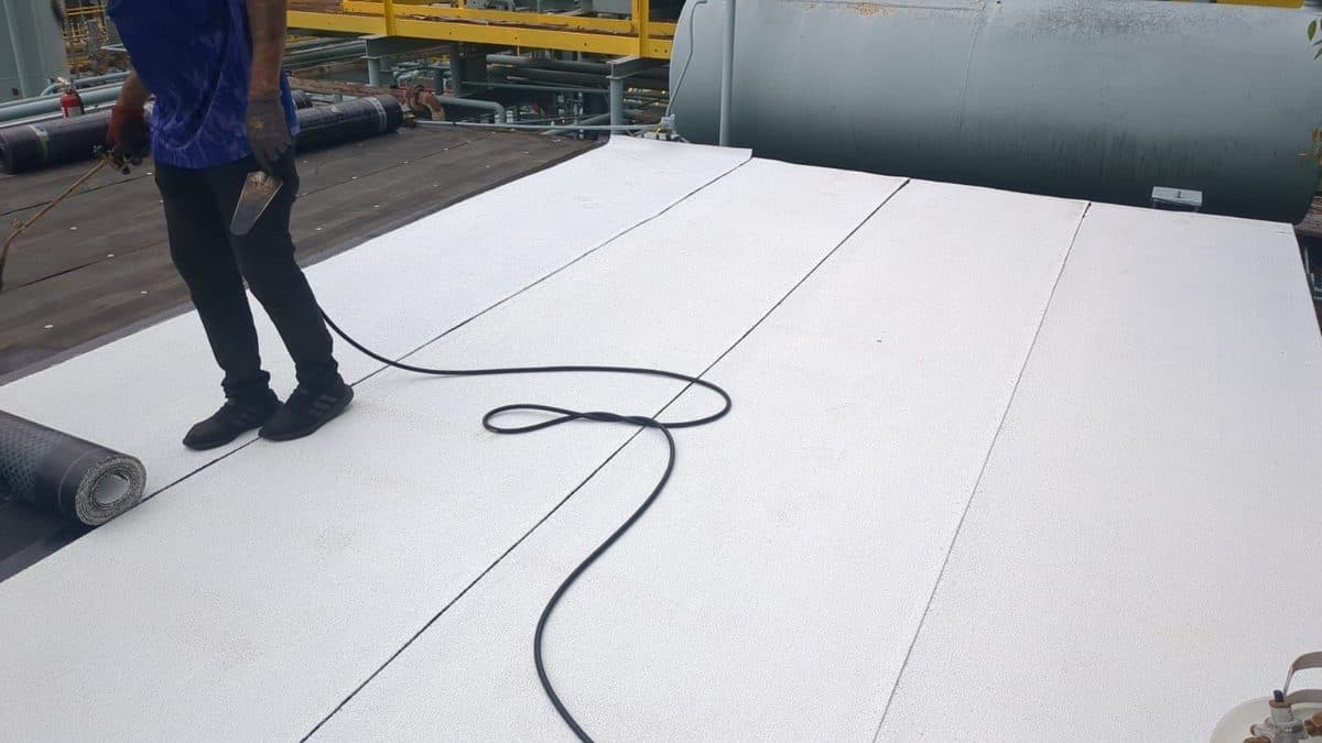 Crew member laying white roofing material on a flat roof beside a roll