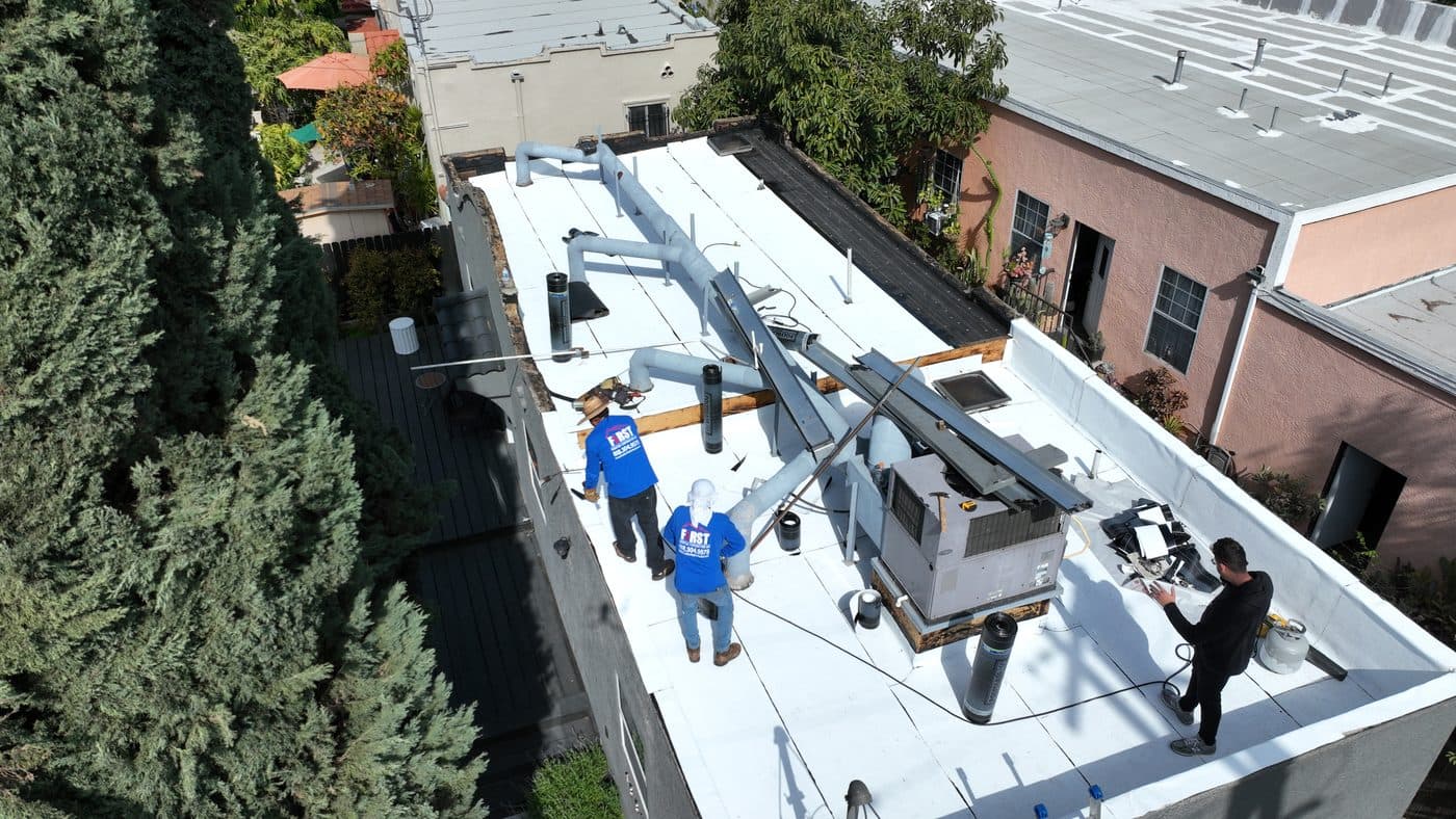 Crew members working around rooftop equipment on a white commercial flat roof