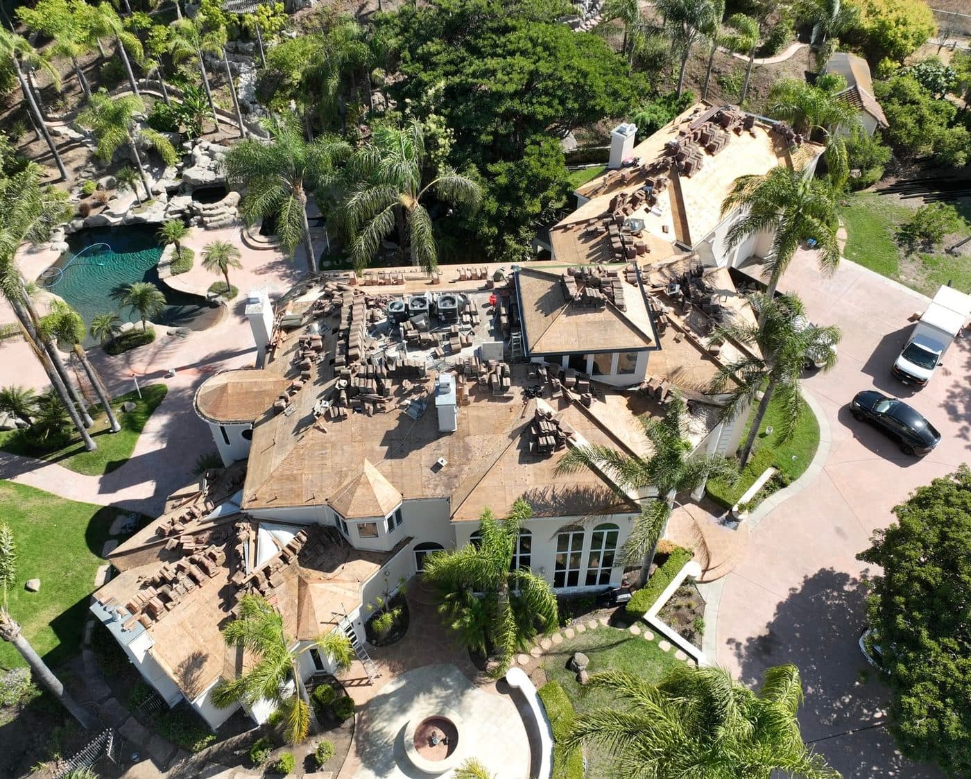 Aerial view of a home mid roof-replacement, with sheathing exposed and new shingles staged for installation