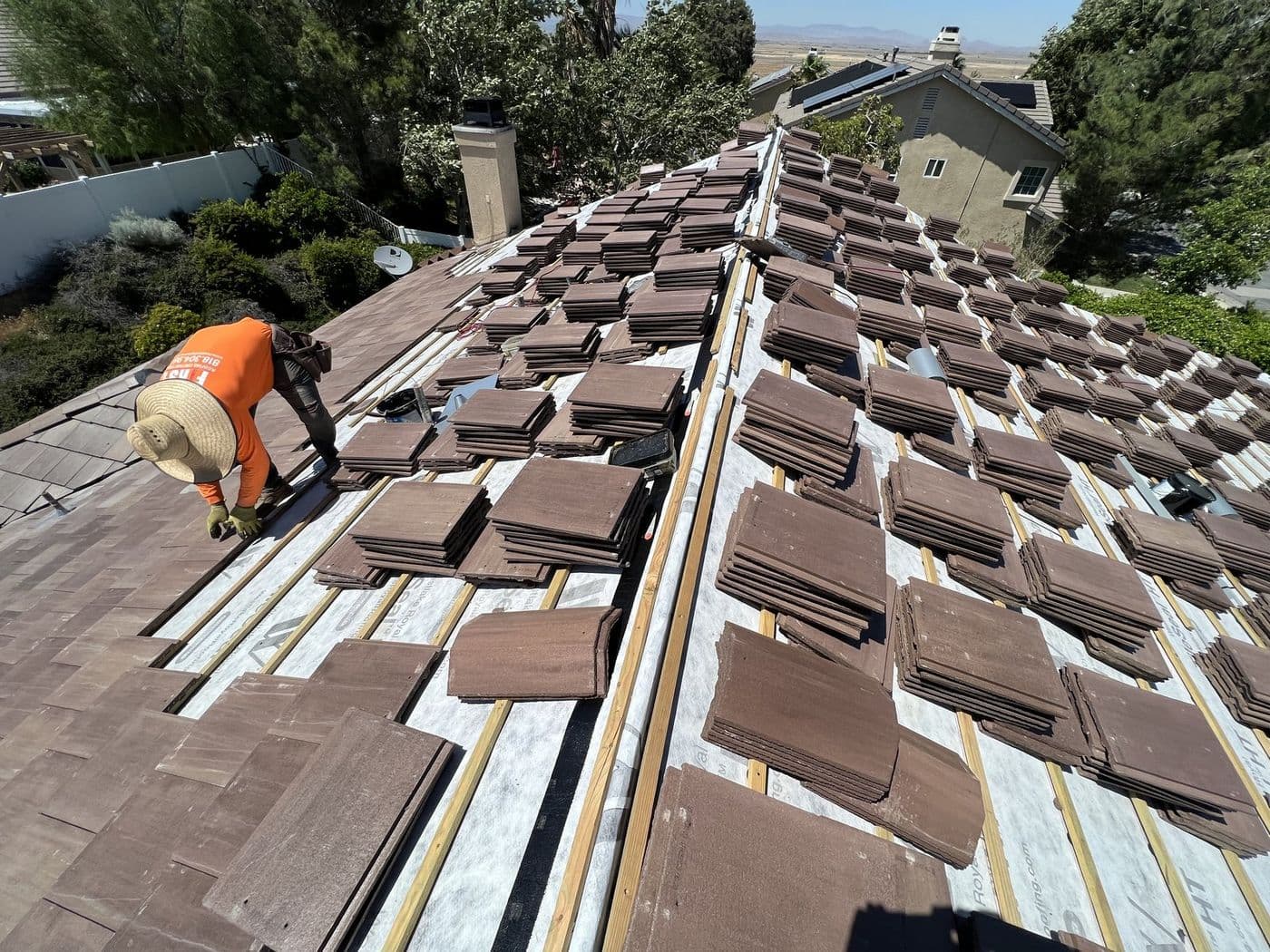 Roofer installing a tile roof, with underlayment and battens laid and tile staged across the roof