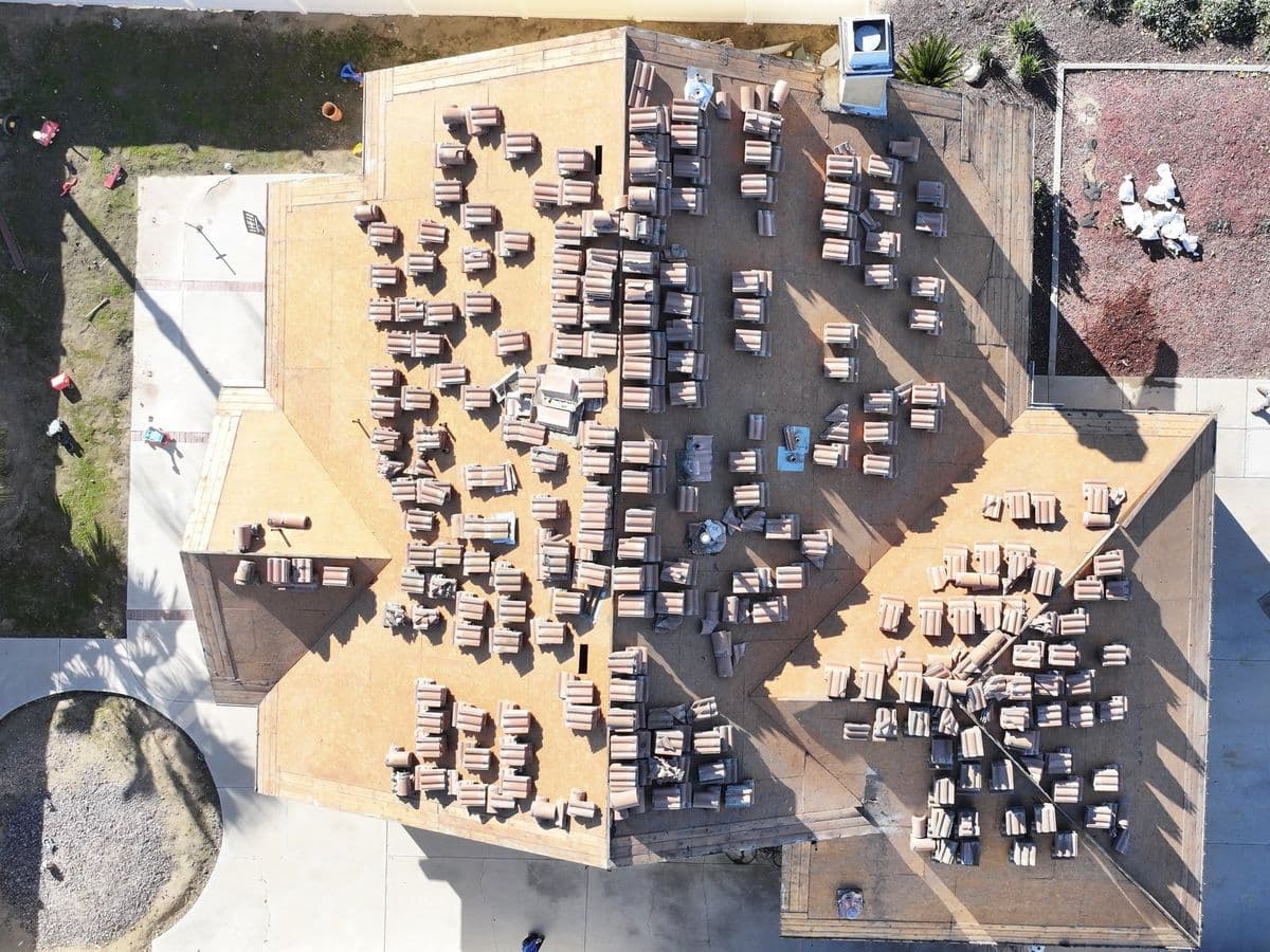 Aerial view of a roof stripped to the deck with tile staged in stacks across it during a re-tile