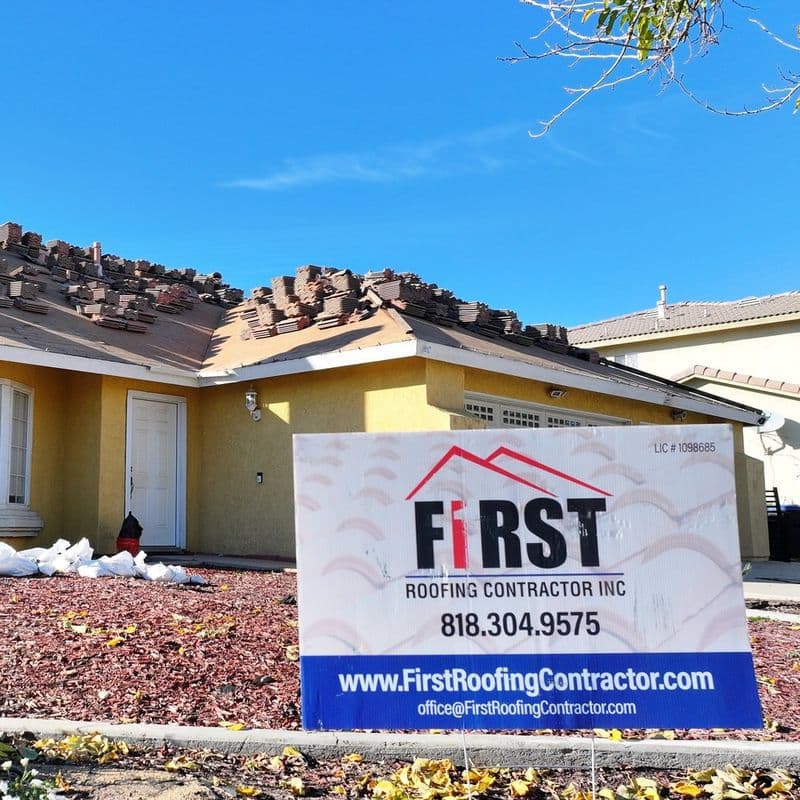 Home with tile staged on the roof and a First Roofing Contractor job-site sign in the yard